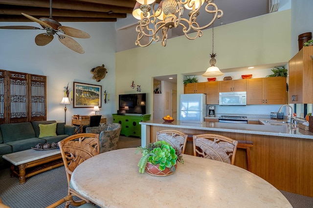 carpeted dining area with sink, a high ceiling, ceiling fan with notable chandelier, and beamed ceiling