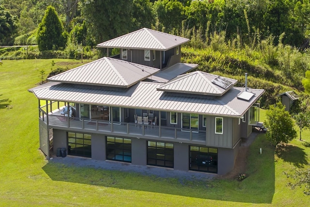 back of house with a standing seam roof, a balcony, a lawn, and metal roof