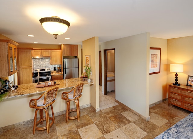 kitchen with appliances with stainless steel finishes, backsplash, a kitchen bar, light stone counters, and kitchen peninsula