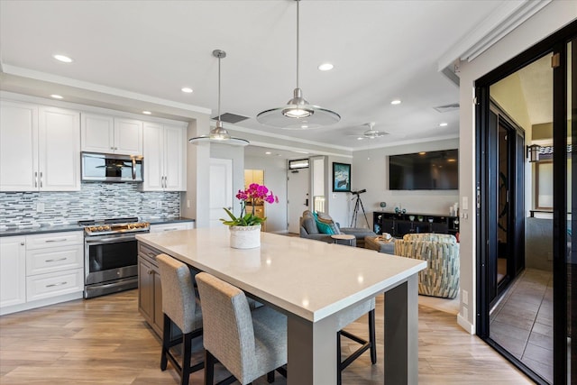 kitchen featuring pendant lighting, a kitchen breakfast bar, ceiling fan, white cabinetry, and stainless steel appliances