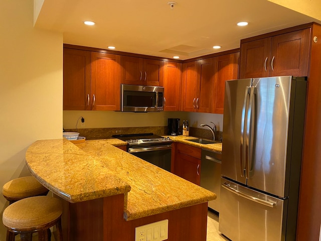 kitchen with kitchen peninsula, a breakfast bar area, light stone countertops, sink, and stainless steel appliances