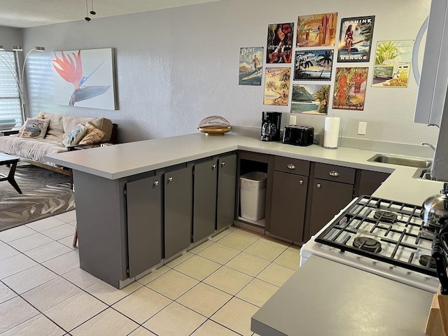 kitchen featuring light tile patterned flooring, kitchen peninsula, white gas range oven, and sink