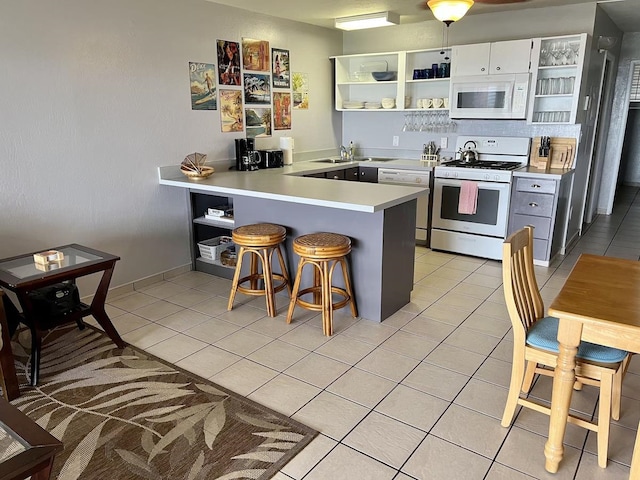 kitchen featuring white appliances, a kitchen bar, white cabinetry, kitchen peninsula, and light tile patterned floors