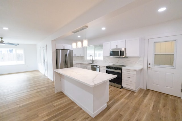 kitchen with sink, appliances with stainless steel finishes, white cabinetry, tasteful backsplash, and decorative light fixtures