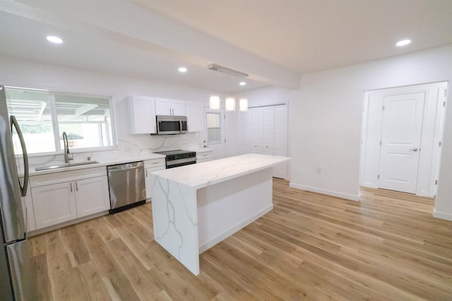 kitchen with sink, appliances with stainless steel finishes, white cabinetry, light stone countertops, and a kitchen island