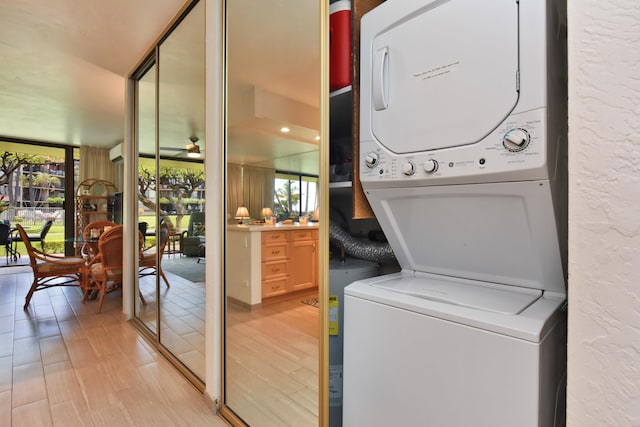 laundry area with a wealth of natural light, light hardwood / wood-style flooring, stacked washing maching and dryer, and ceiling fan