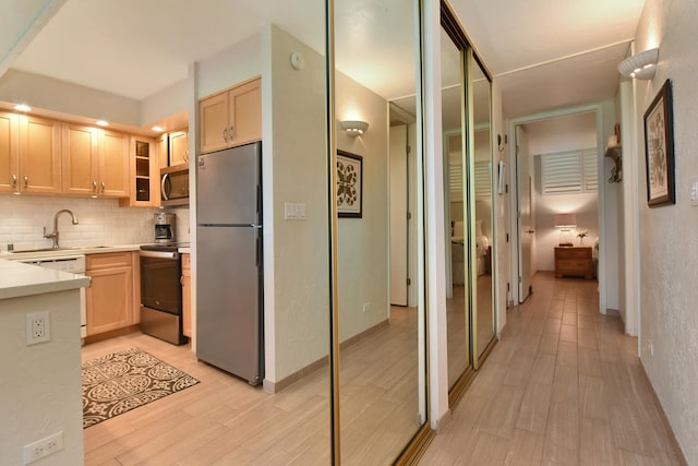 kitchen featuring backsplash, stainless steel appliances, light brown cabinetry, and light wood-type flooring