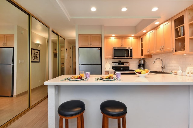 kitchen featuring appliances with stainless steel finishes, light hardwood / wood-style floors, a kitchen bar, tasteful backsplash, and sink