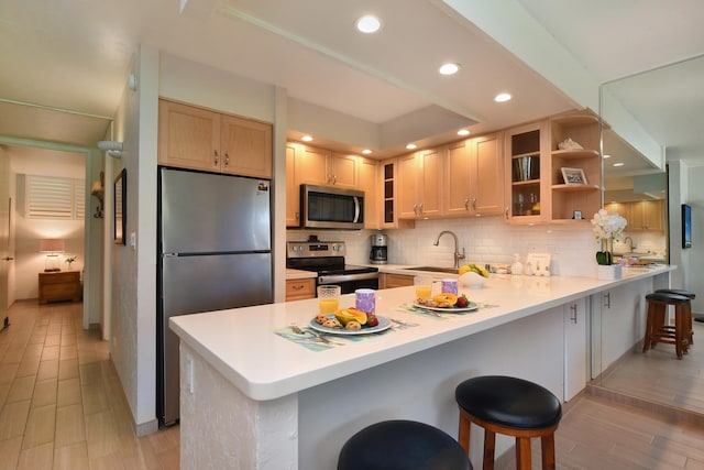 kitchen with a breakfast bar, sink, appliances with stainless steel finishes, decorative backsplash, and light hardwood / wood-style floors