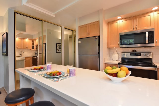 kitchen with backsplash, wood-type flooring, light brown cabinets, a breakfast bar area, and stainless steel appliances