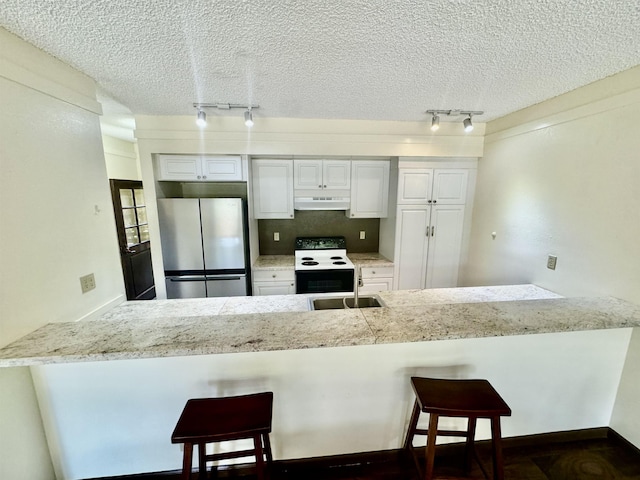 kitchen with white cabinets, stainless steel fridge, a kitchen breakfast bar, track lighting, and electric stove