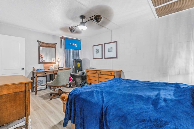 bedroom featuring light wood-type flooring, a ceiling fan, a textured ceiling, and concrete block wall