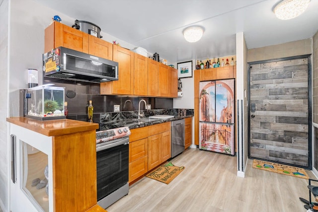 kitchen with dark stone counters, appliances with stainless steel finishes, backsplash, light wood-style floors, and a sink