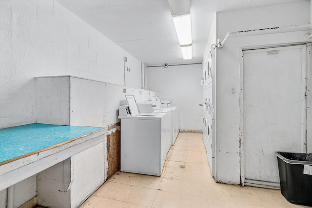 common laundry area featuring concrete block wall, light floors, washer and dryer, and stacked washer / drying machine