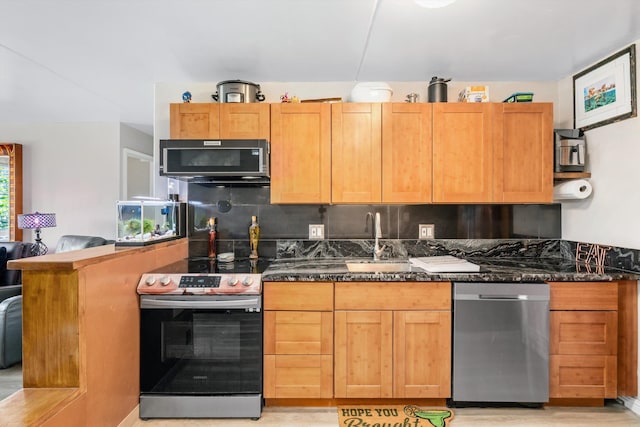 kitchen with appliances with stainless steel finishes, backsplash, dark stone countertops, and a sink