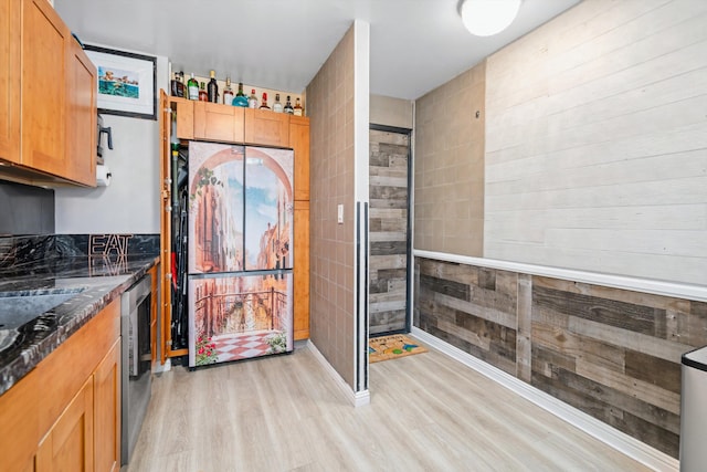 kitchen featuring light wood-style flooring, dark stone counters, dishwasher, and freestanding refrigerator