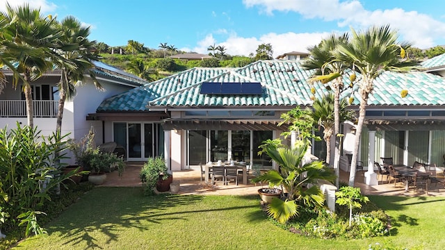 rear view of house featuring roof mounted solar panels, a patio area, a lawn, and a pergola