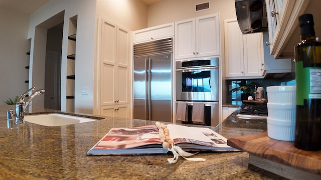 kitchen with stainless steel appliances, visible vents, white cabinets, a sink, and dark stone counters