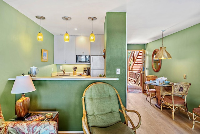 kitchen featuring white refrigerator, decorative light fixtures, white cabinetry, and black microwave