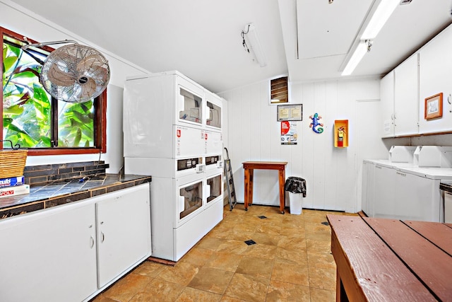 kitchen with white cabinets, washer and dryer, stacked washer / dryer, and wooden walls