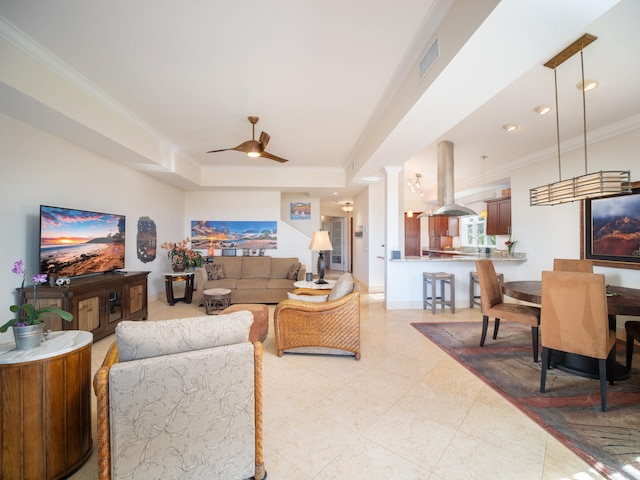 living room with a raised ceiling, ceiling fan, decorative columns, and ornamental molding