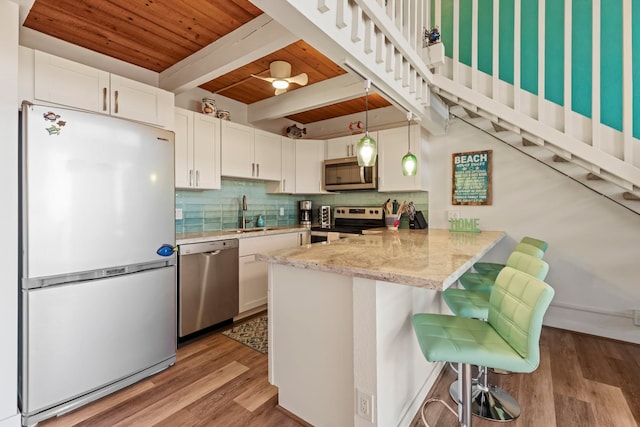 kitchen featuring pendant lighting, wood ceiling, kitchen peninsula, appliances with stainless steel finishes, and a breakfast bar area