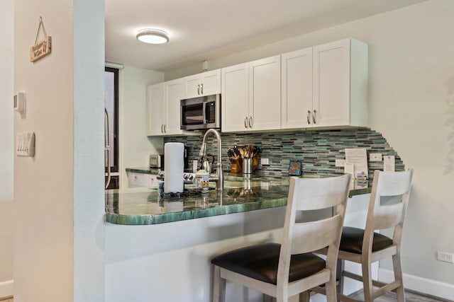 kitchen featuring white cabinets, a breakfast bar area, backsplash, kitchen peninsula, and stove