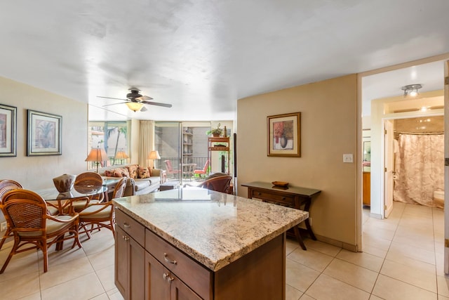 kitchen with light stone countertops, a kitchen island, ceiling fan, and light tile patterned flooring