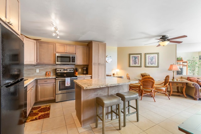 kitchen with light brown cabinets, backsplash, light stone countertops, a kitchen island, and stainless steel appliances