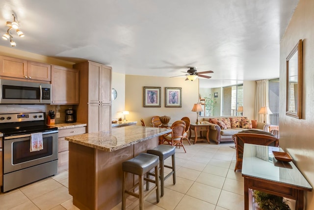 kitchen with a breakfast bar, a center island, ceiling fan, light stone countertops, and stainless steel appliances