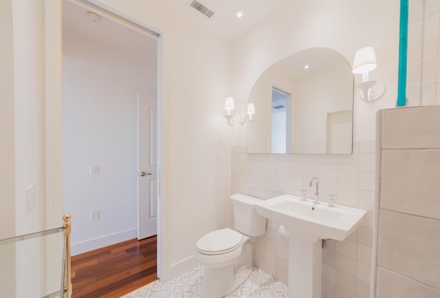 bathroom featuring toilet, wood-type flooring, and tile walls