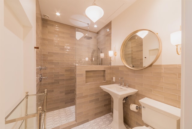 bathroom with a tile shower, toilet, tile walls, and tile patterned floors