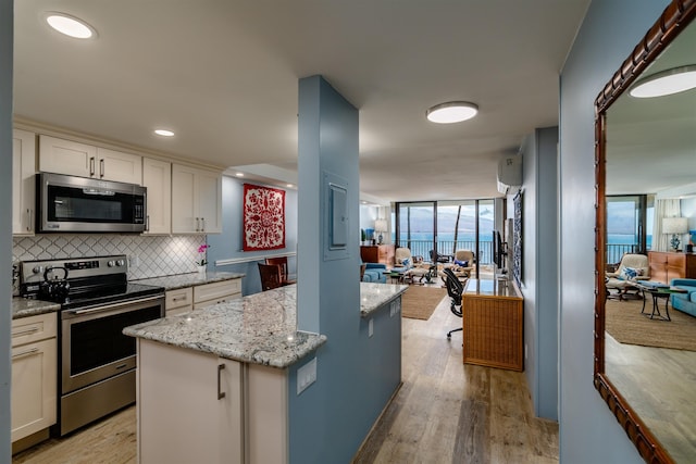 kitchen with decorative backsplash, light stone countertops, light wood-style floors, open floor plan, and appliances with stainless steel finishes