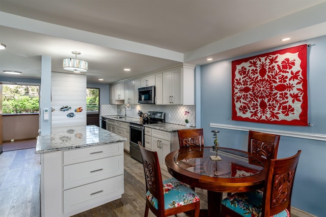 kitchen featuring backsplash, wood finished floors, light stone counters, white cabinets, and stainless steel appliances