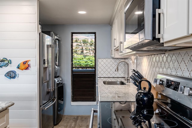 kitchen featuring decorative backsplash, stacked washer and dryer, appliances with stainless steel finishes, a sink, and light wood-style floors