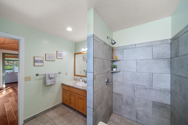 full bath with a tile shower, vanity, and baseboards