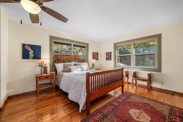 bedroom featuring wood-type flooring, multiple windows, baseboards, and a ceiling fan