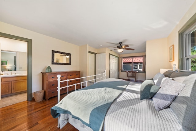 bedroom with a sink, ensuite bath, multiple windows, and wood finished floors