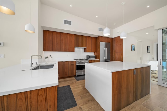 kitchen with sink, premium appliances, tasteful backsplash, light hardwood / wood-style floors, and pendant lighting