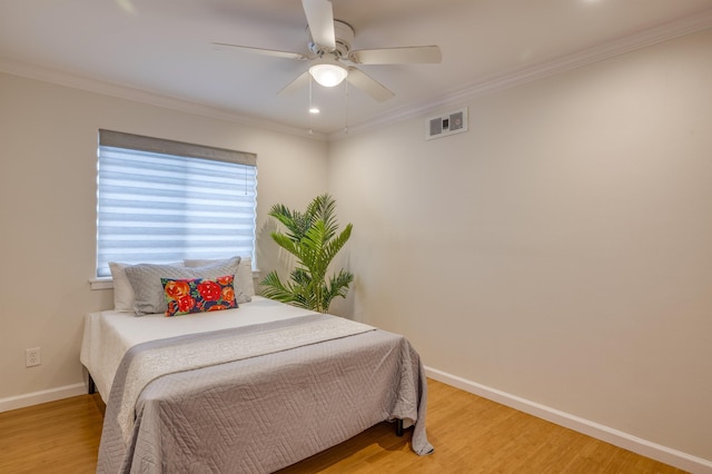 bedroom with ceiling fan, wood finished floors, visible vents, baseboards, and crown molding