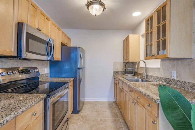 kitchen featuring light stone counters, stainless steel appliances, tasteful backsplash, glass insert cabinets, and a sink