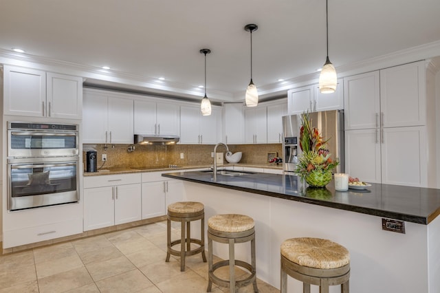 kitchen featuring stainless steel appliances, a breakfast bar, a sink, white cabinetry, and dark countertops