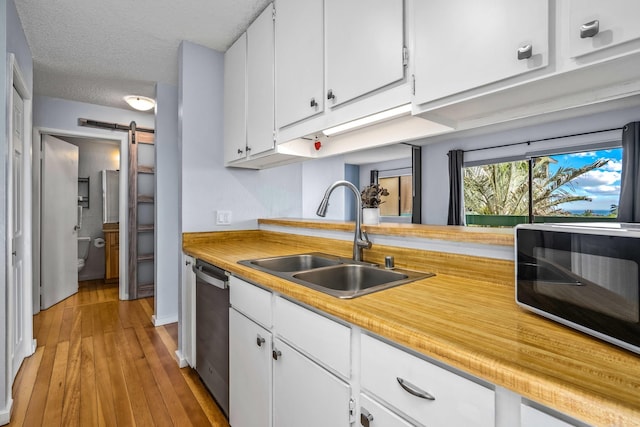 kitchen with stainless steel dishwasher, a textured ceiling, sink, a barn door, and white cabinets