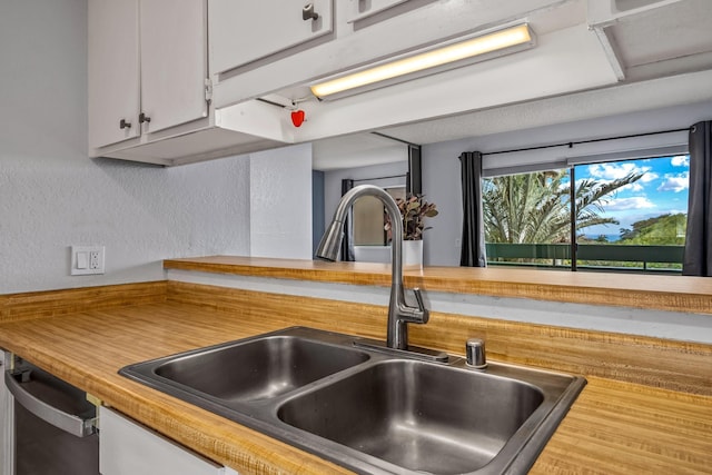 kitchen featuring dishwashing machine, white cabinetry, and sink