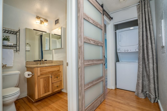 bathroom featuring vanity, a textured ceiling, hardwood / wood-style floors, toilet, and stacked washer / drying machine