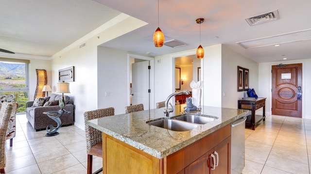 kitchen with a center island with sink, pendant lighting, a kitchen bar, sink, and light stone countertops