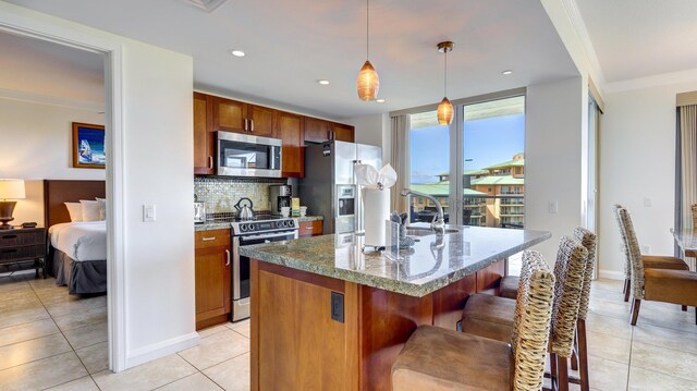 kitchen with pendant lighting, decorative backsplash, light tile patterned flooring, an island with sink, and stainless steel appliances