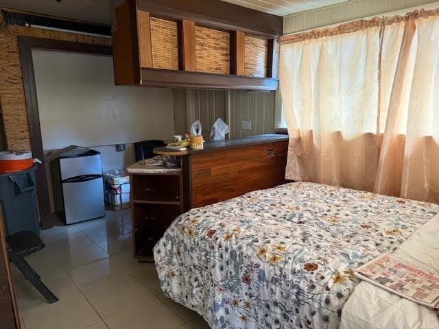 bedroom with freestanding refrigerator and light tile patterned flooring