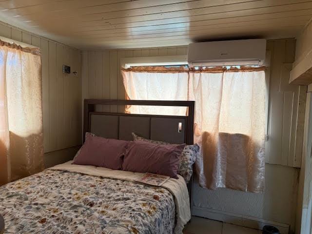tiled bedroom with an AC wall unit, multiple windows, and wooden ceiling
