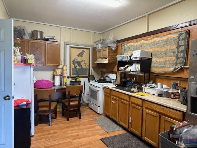 kitchen with white gas range oven, under cabinet range hood, brown cabinets, light countertops, and light wood finished floors